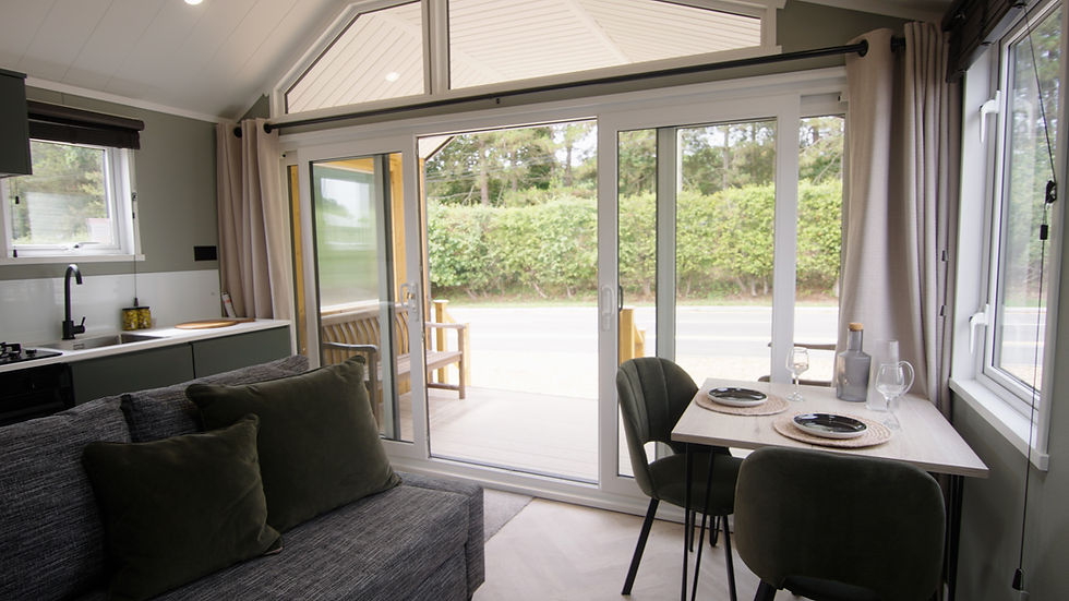 The open plan living area of a holiday home, with sliding doors open, showing trees beyond.