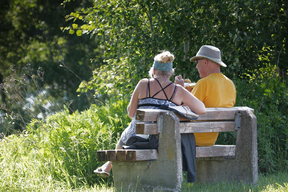 A couple sitting on a bench having something to eat in the sunshine.