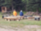 Two people sitting outside on log bench with their back to the camera in prayer