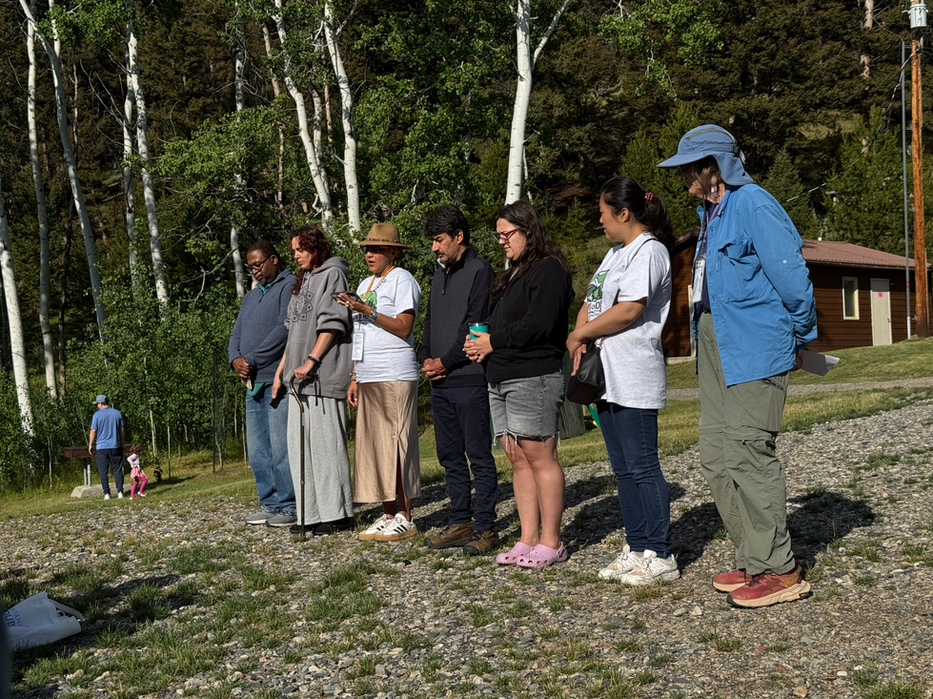 seven adults standing in a line with hands clasped at waists in prayer