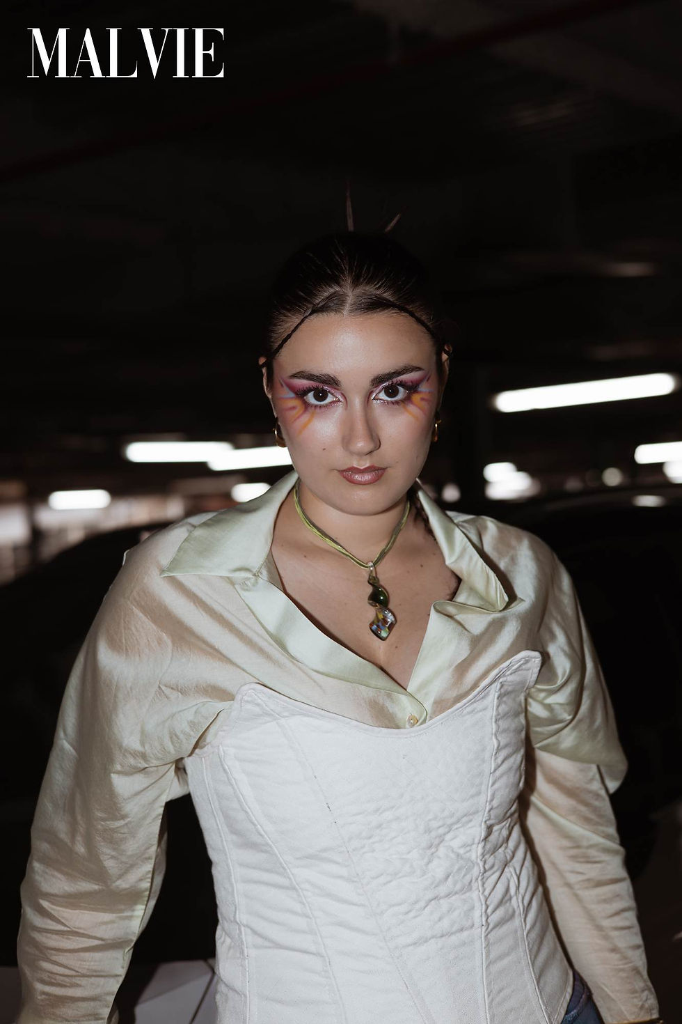 Close portrait of the model in a white corset and satin shirt with a pendant and pink-and-violet eye make-up