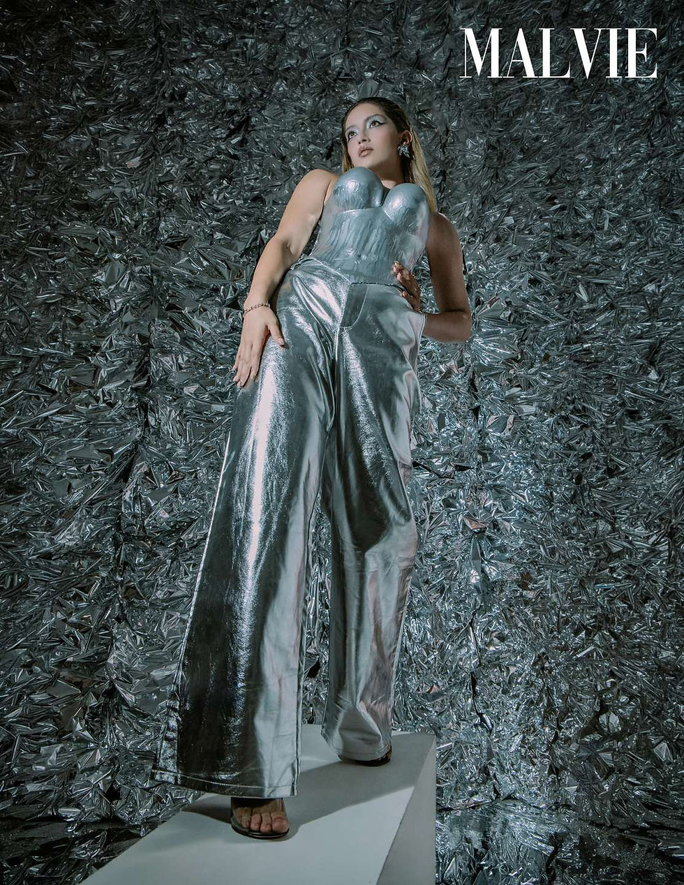 Full-length model in the silver corset and wide metallic trousers standing on a white plinth