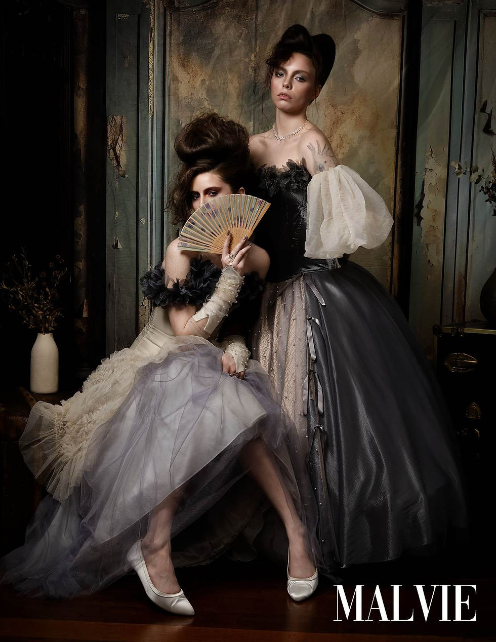 The two models together, one hiding behind a painted fan, the other standing in pewter satin