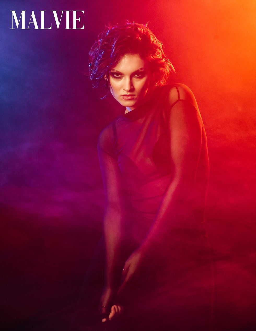 Model leaning forward in red and orange light, blue haze to one side