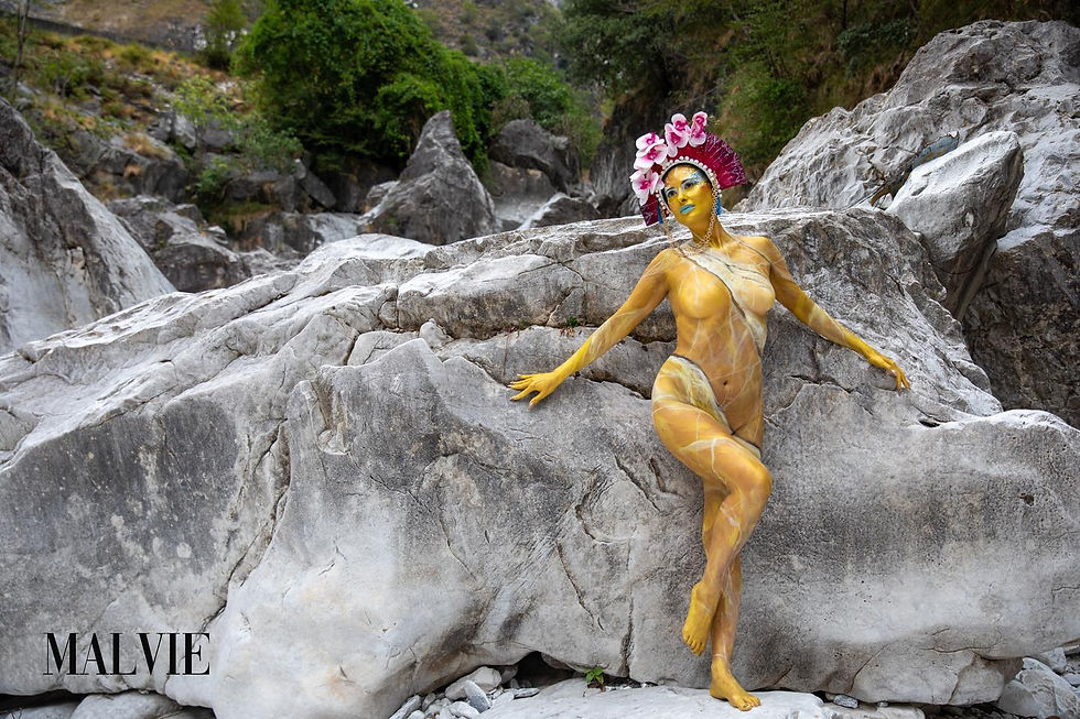 Gold-painted model with an orchid crown posing against a sloping rock face