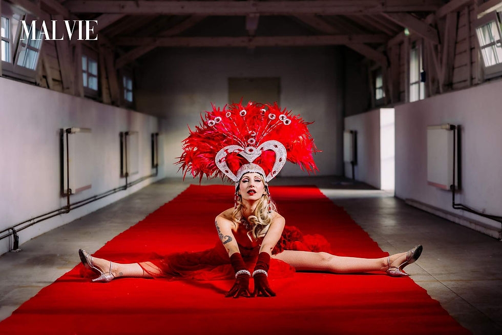 Model doing the splits on a long red carpet in an empty loft, wearing the feathered headdress