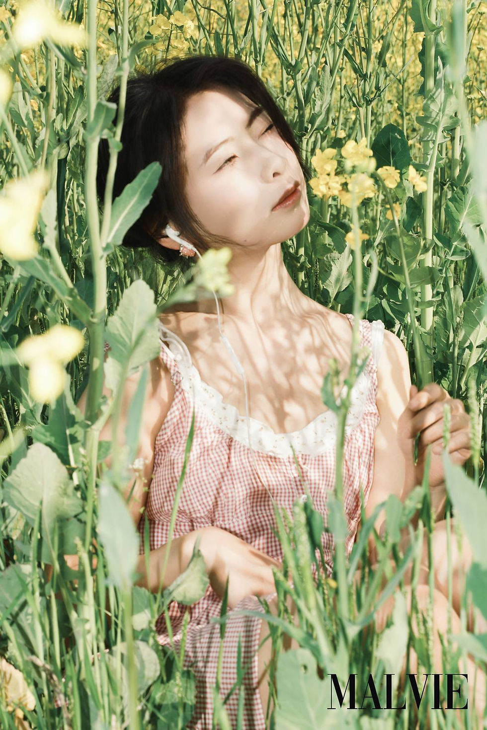 Woman with closed eyes among yellow flowers, sunlight on a pink dress