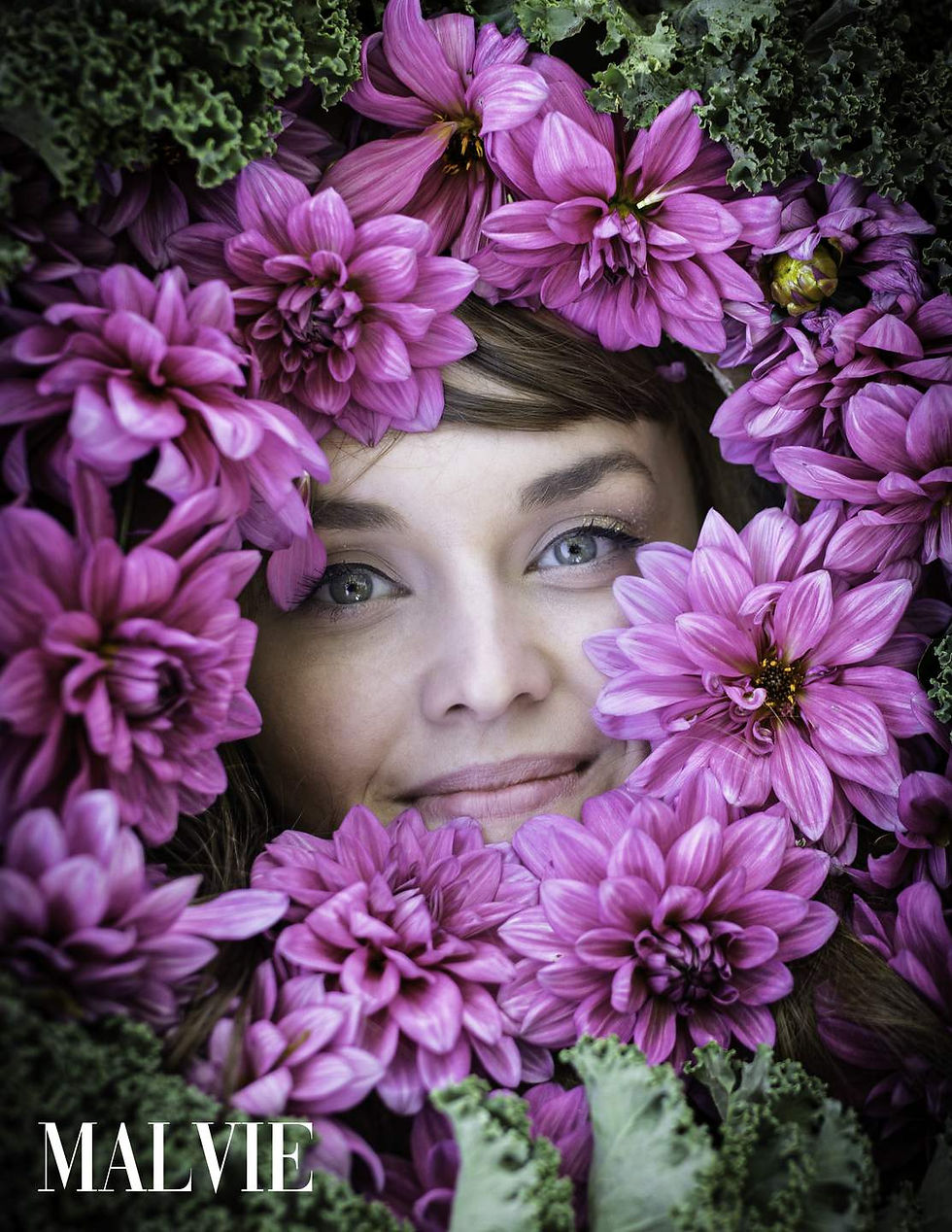 Model looking up at the camera, her face framed by purple dahlias and green kale