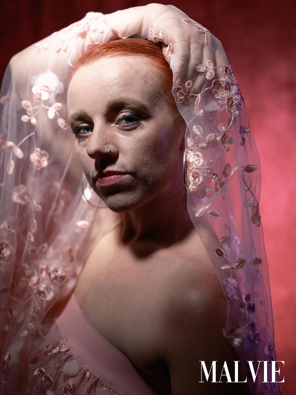 Close portrait with copper hair, one arm over her head holding the lace veil