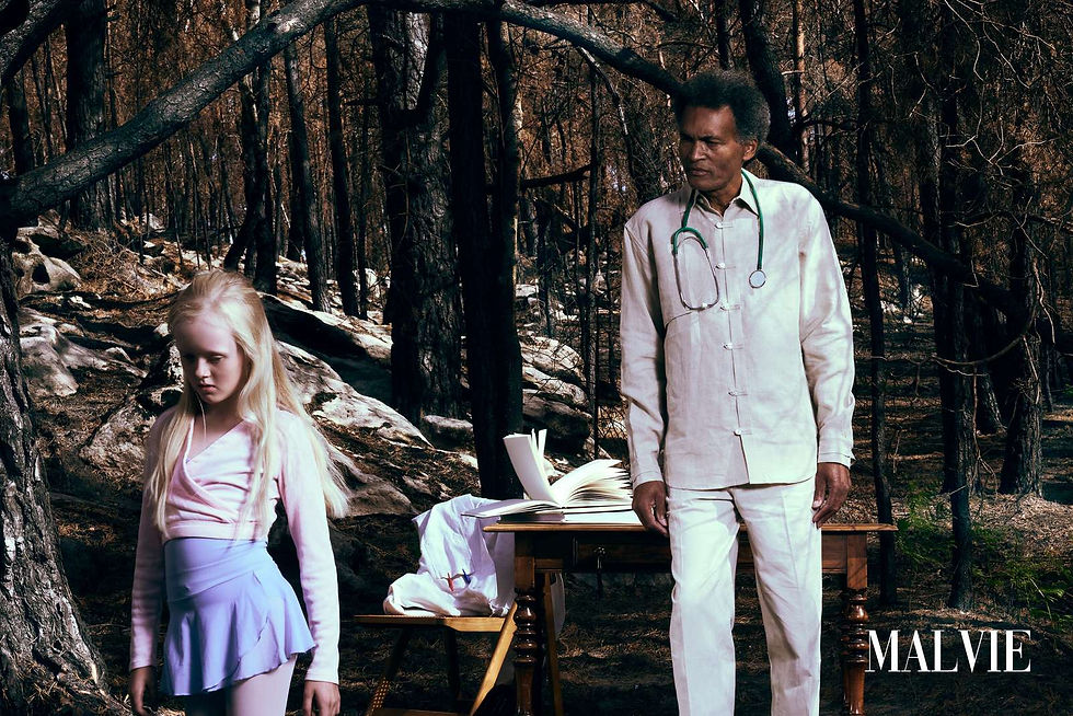 Girl with white-blonde hair in a pink wrap top beside a man in white with a stethoscope in a burnt forest