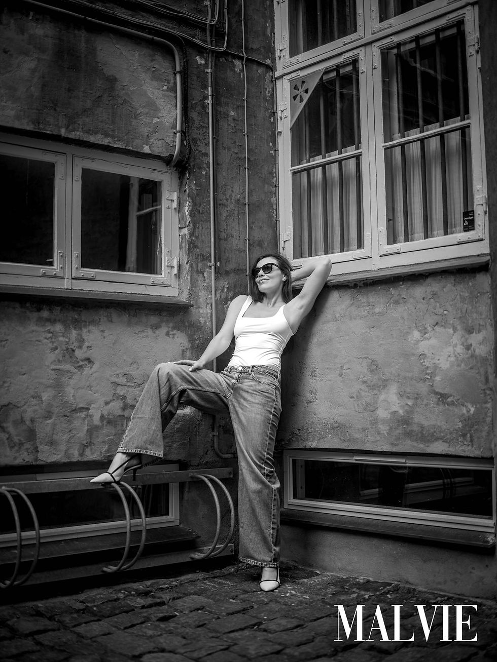 Model in sunglasses leaning on a weathered wall under barred windows