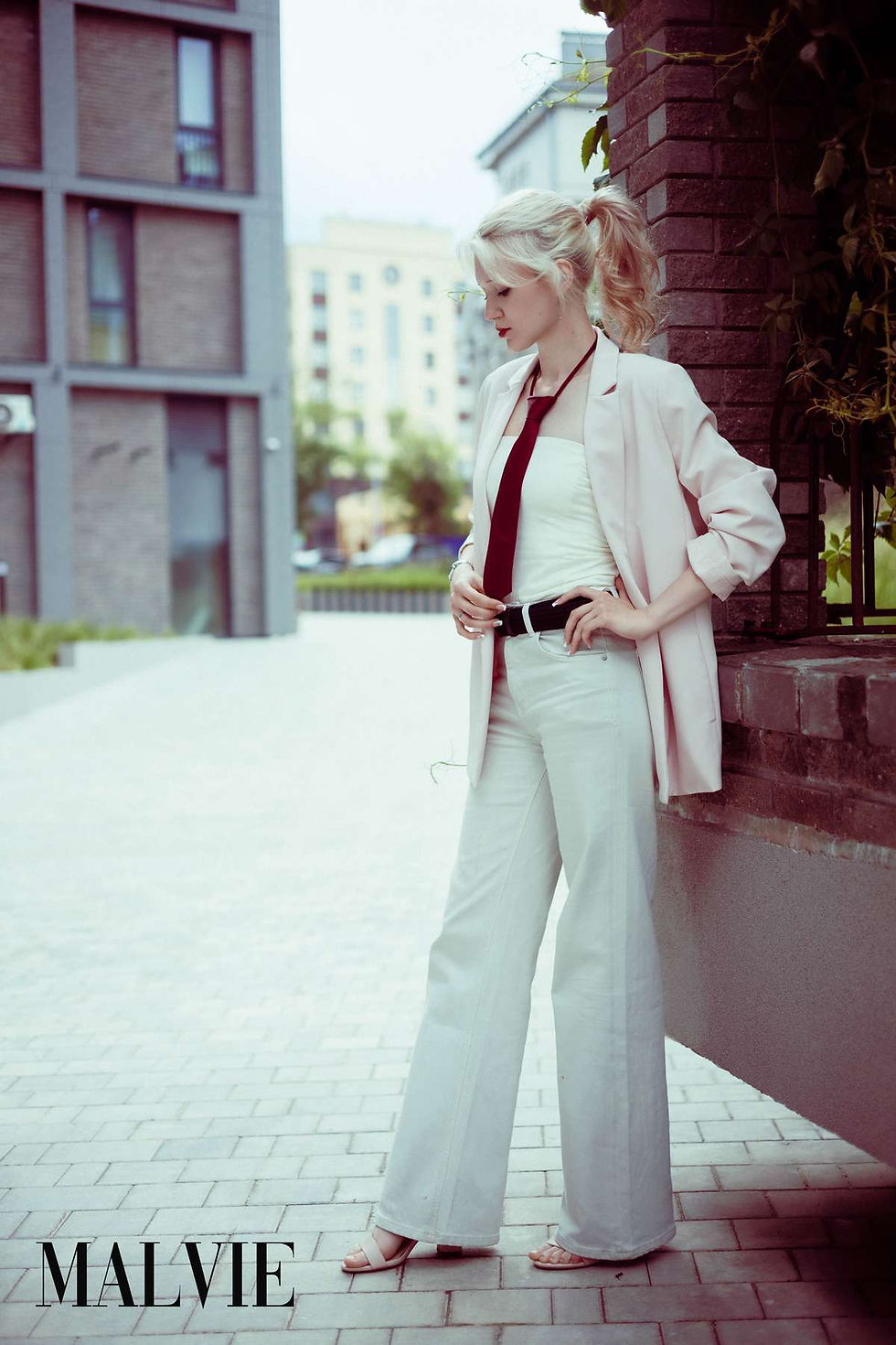 Model in a pale pink blazer and white wide-leg trousers on a paved street by modern buildings