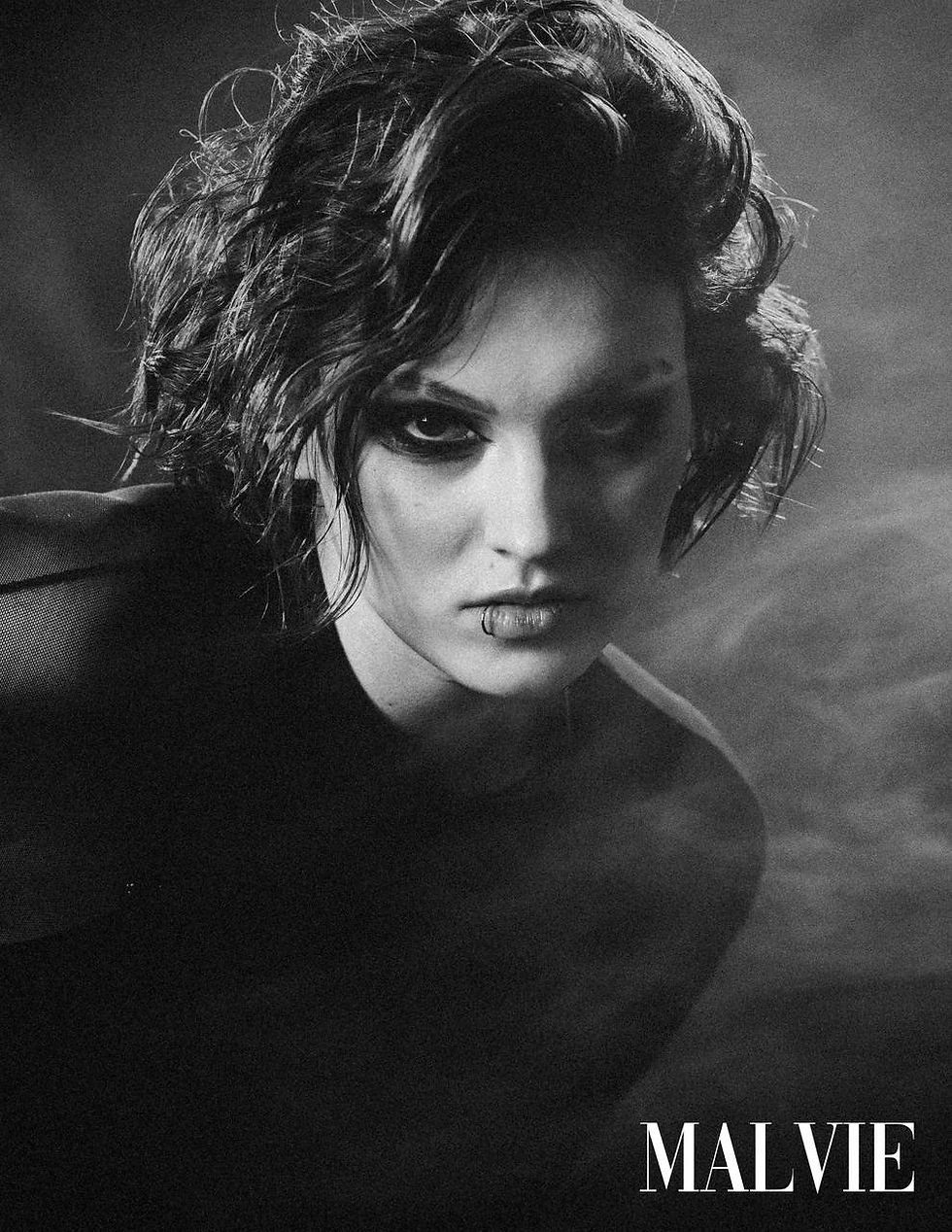 Black-and-white portrait of the model with tousled curls looking down, smoke behind