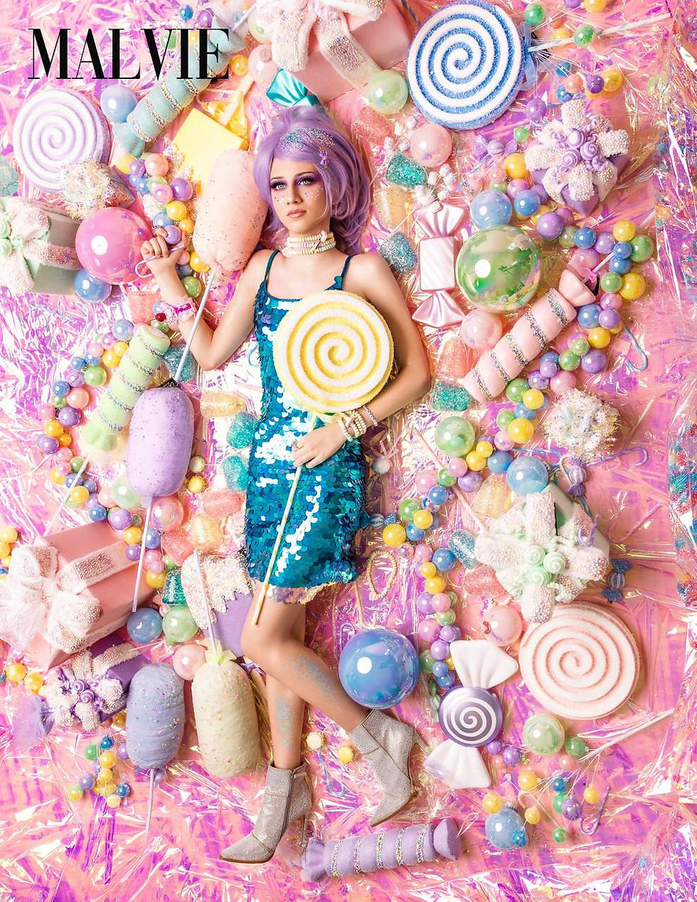 Model in a lilac wig and turquoise sequin dress holding a swirl lollipop, seen from above