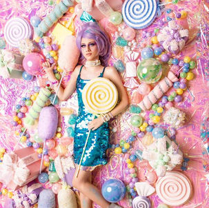 Model in a lilac wig and a turquoise sequin dress holding a giant lollipop among pastel candies – Le Bonbon by Kristia Knowles for MALVIE Magazine