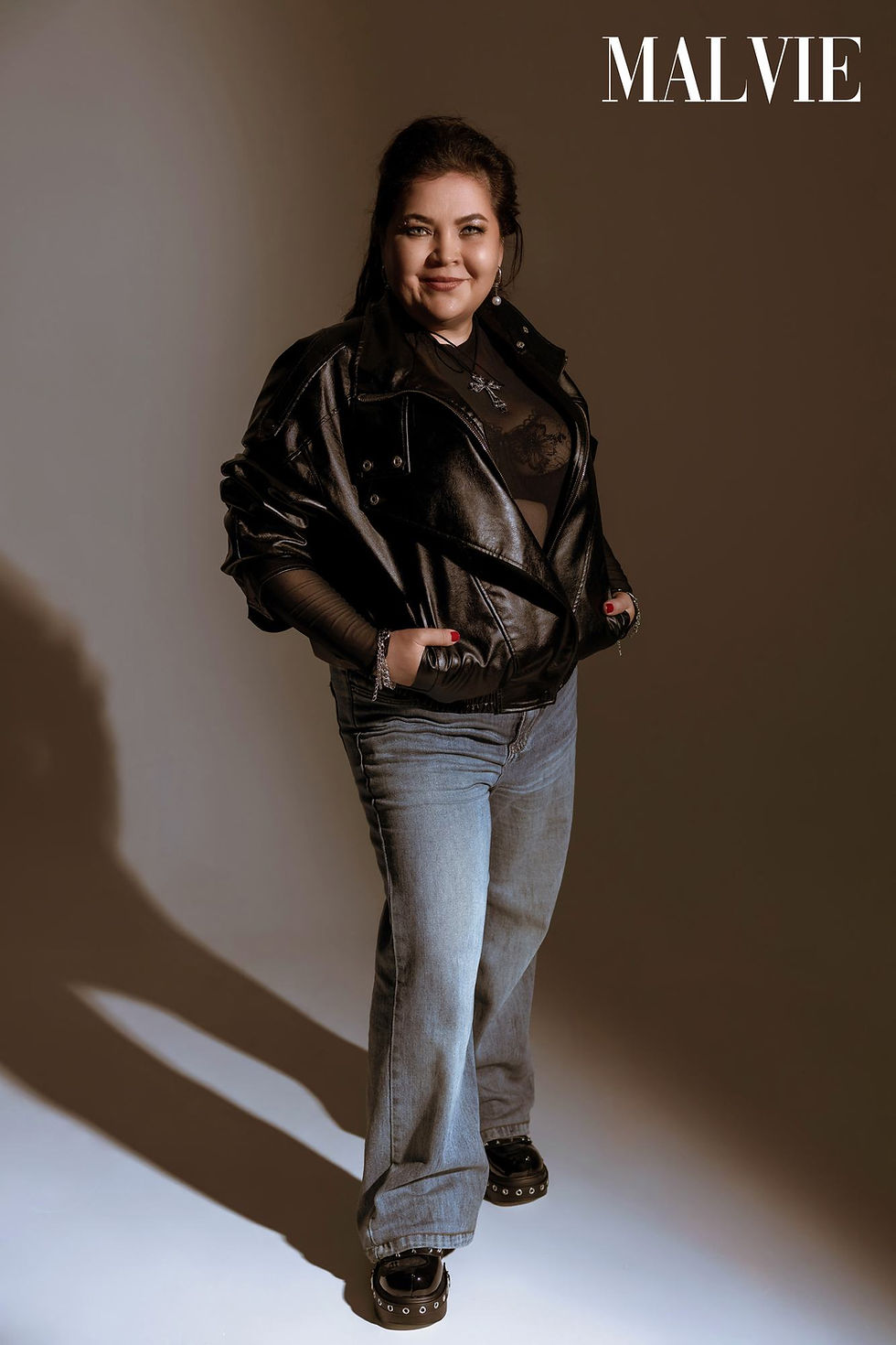 Model standing in a black leather jacket and light-wash jeans against a beige wall