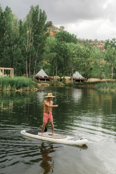 Man paddle boarding in a straw hat and orange swim suit at Cave Lakes Canyon resort.