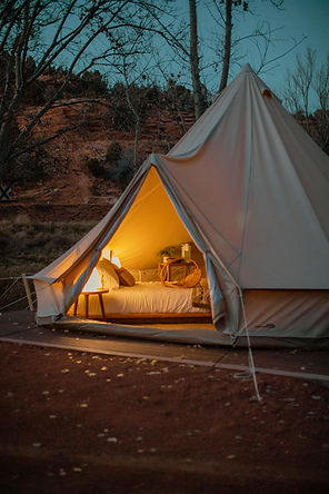 A canvas glamping tent with an open door illuminating light as the sun has gone down behind a hill at Cave Lakes resort..