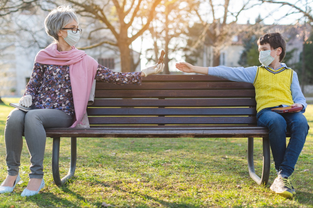 grandmother and grandson wearing masks sitting apart on a bench