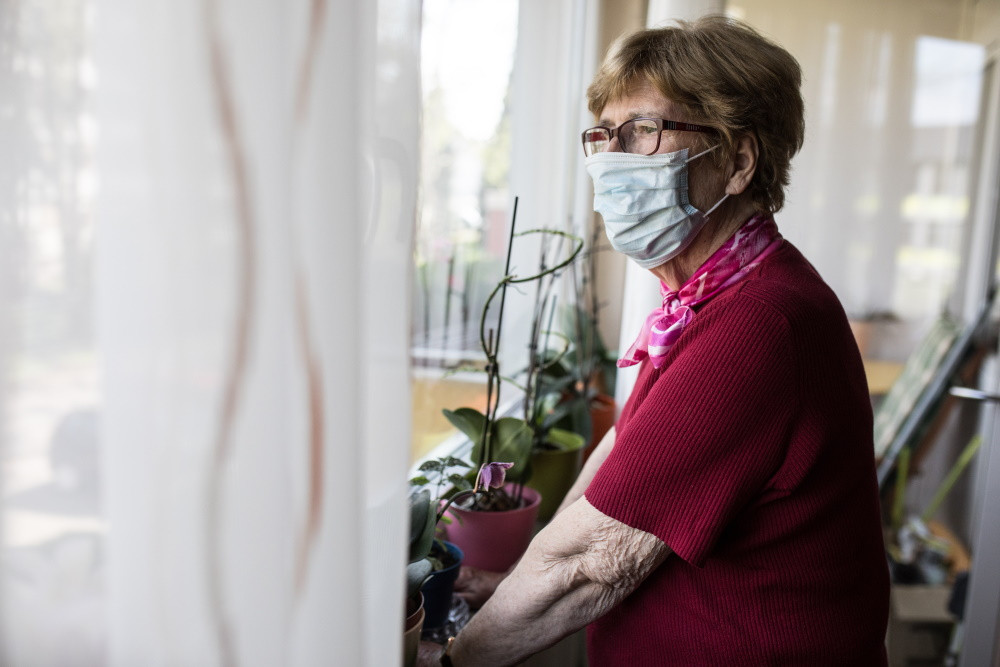 senior woman in mask looking out window