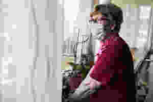 senior woman in mask looking out window