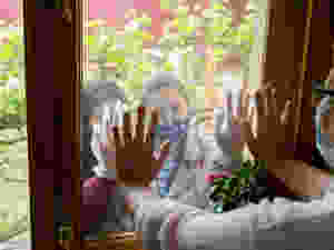 Senior looking through window at grandchildren wearing masks