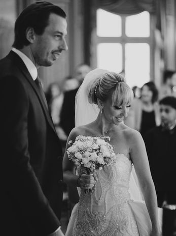Mariée en robe ornée tenant son bouquet de fleurs, entourée d’invités lors de la cérémonie de mariage.