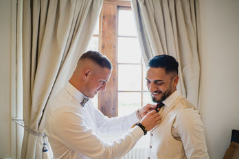 Photos des préparatifs du marié – l'ami aide à ajuster la cravate, ambiance détendue et élégante avant le grand jour.