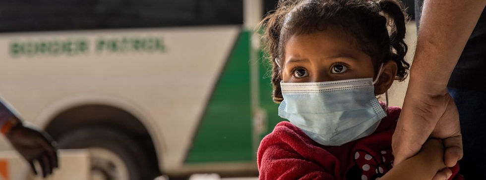 Child in mask holds her parent's hand. Border Patrol van is in the background.