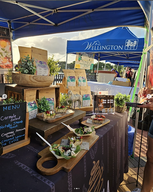 Carmela Coffee stand, menu, snacks, plants, Wellington tent visible, assorted food items displayed.