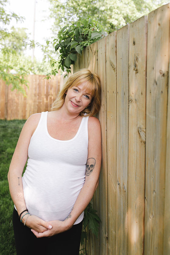 Amy leaning against fence, outdoors surrounded by greenery