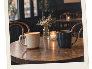Two coffee mugs facing each other at an empty cafe table.