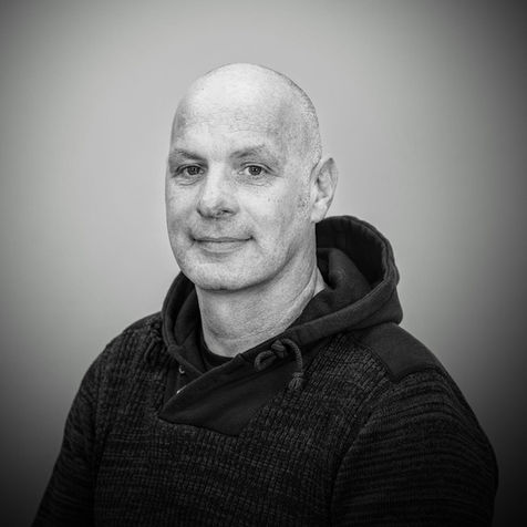Middle aged man smiling wearing a dark coloured jumper with a hood.