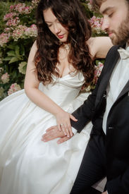Bride and groom sitting closely together during an outdoor summer wedding, holding hands and looking down in soft light.