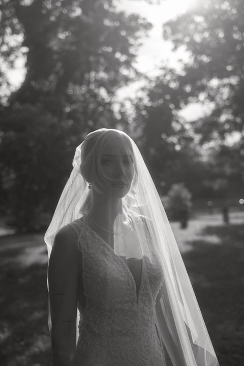 Bride wearing a veil standing outdoors during a summer wedding at a historic castle, photographed in black and white.
