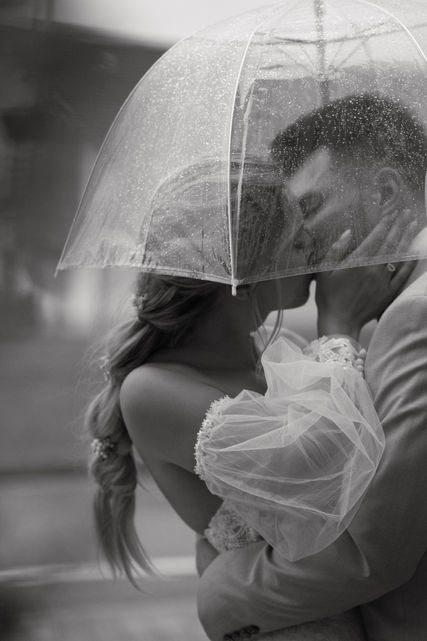 Bride and groom sharing a kiss under an umbrella during their rainy wedding in Altötting, Germany - captured in elegant black and white.