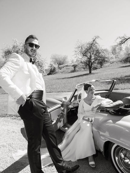 Black and white wedding photo of bride and groom with a vintage Mercedes during their elegant countryside wedding at Gut Aichet Bavaria.