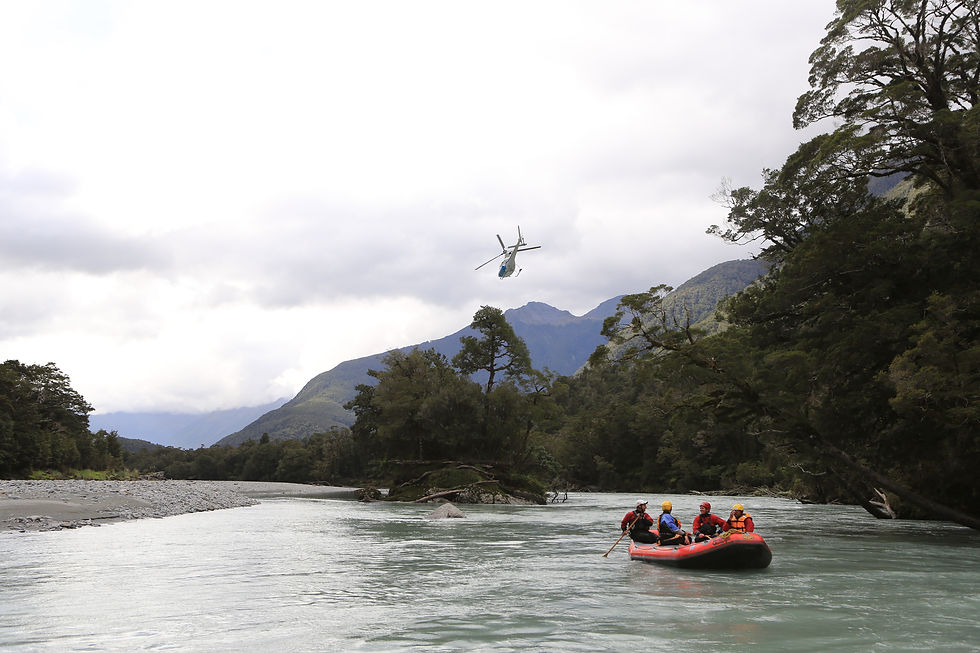 A helicopter flys away while a raft with four people floats down a wilderness river