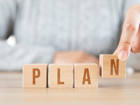 Hand arranges wooden blocks spelling "PLAN" on a wooden surface. Neutral background, soft lighting, focusing on the concept of planning.