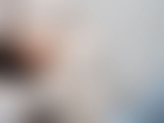 Woman sits on floor near sofa, hands covering face, wearing a cream sweater and ripped jeans. The mood is distressed. White curtains in the background.