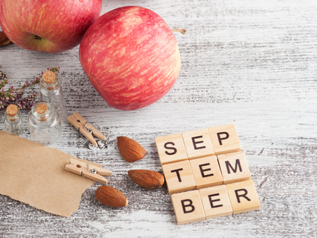 Red apples, almonds, and "September" spelled with wooden tiles on rustic wood. Glass jars and dried flowers add a cozy autumn feel.