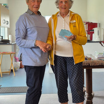 Two women, one in yellow jacket, exchange a small blue card.