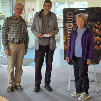 Three people, two men and a woman, standing. One man holds a white envelope.