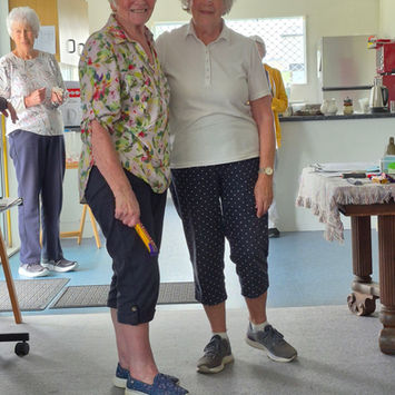 Two older women smiling, one holding a yellow object