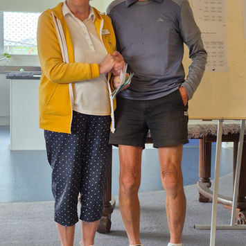 Smiling older woman in yellow jacket holding arm of older man in grey shirt