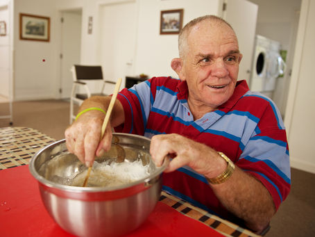 Senior man with a disability at home mixing flour. He was cooking muffins for supper in his kitchen.