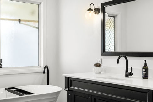 White bath and black vanity with with large black framed mirror