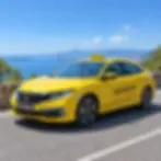 Outdoor photography of a bright yellow taxi parked on a coastal road overlooking the sea. The setting evokes a sense of travel and scenic transportation.