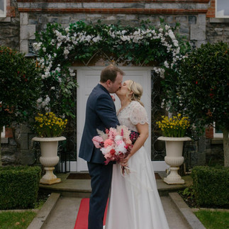 Bride and groom outside Ballymagarvey Village with pink dried wedding bouquet Co Meath Ireland