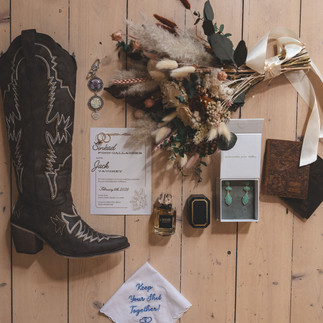 Wedding details with cowboy boots, invitation suite and preserved bridal bouquet.